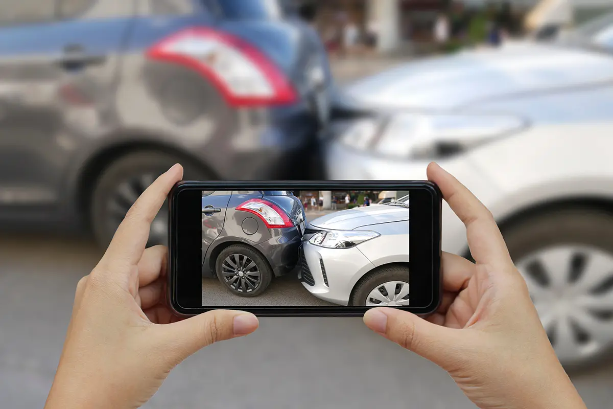 Person using a mobile phone camera to document side panel damage on a vehicle.