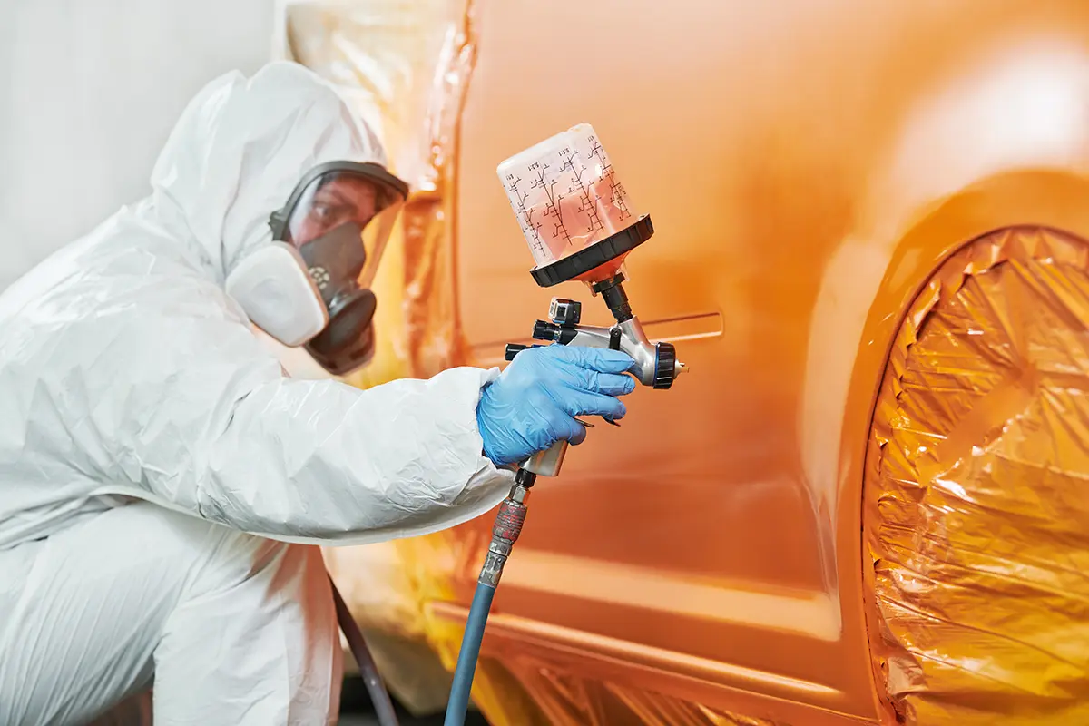 Professional collision repair painter applying perfectly matched orange paint to a vehicle.