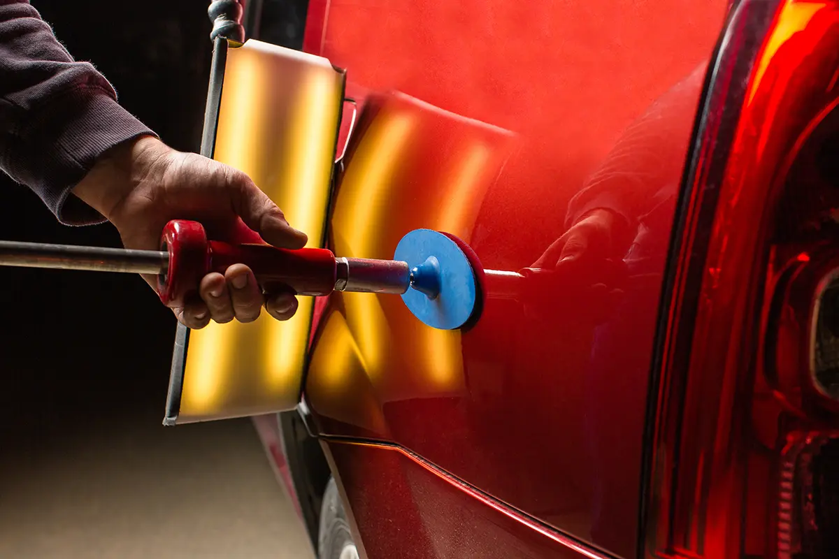Close-up of specialized tools being used to repair a dent on a red car.