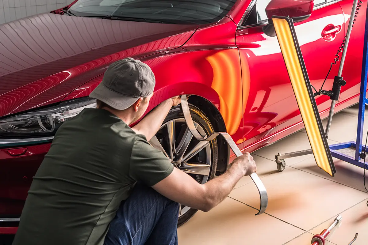 Technician using a specialized light board to perform paintless dent repair on a red car.