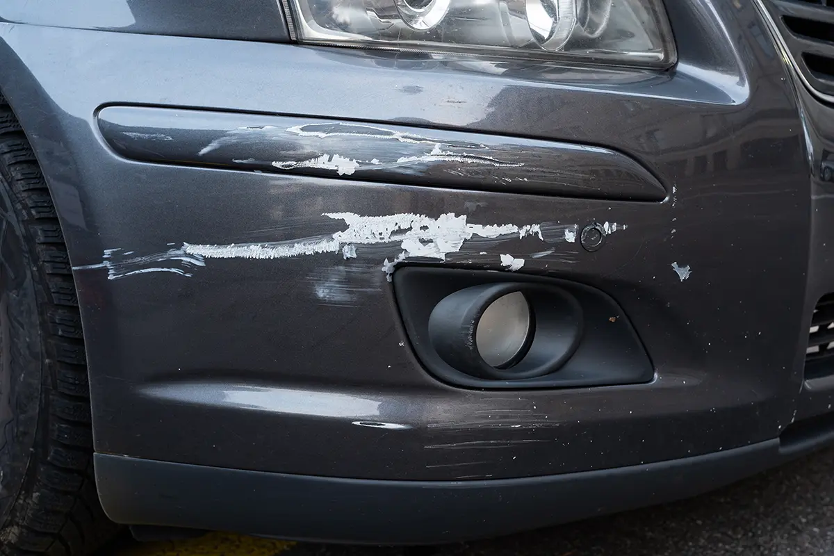 Close up showing collision damage and scraped paint on a car's front bumper.