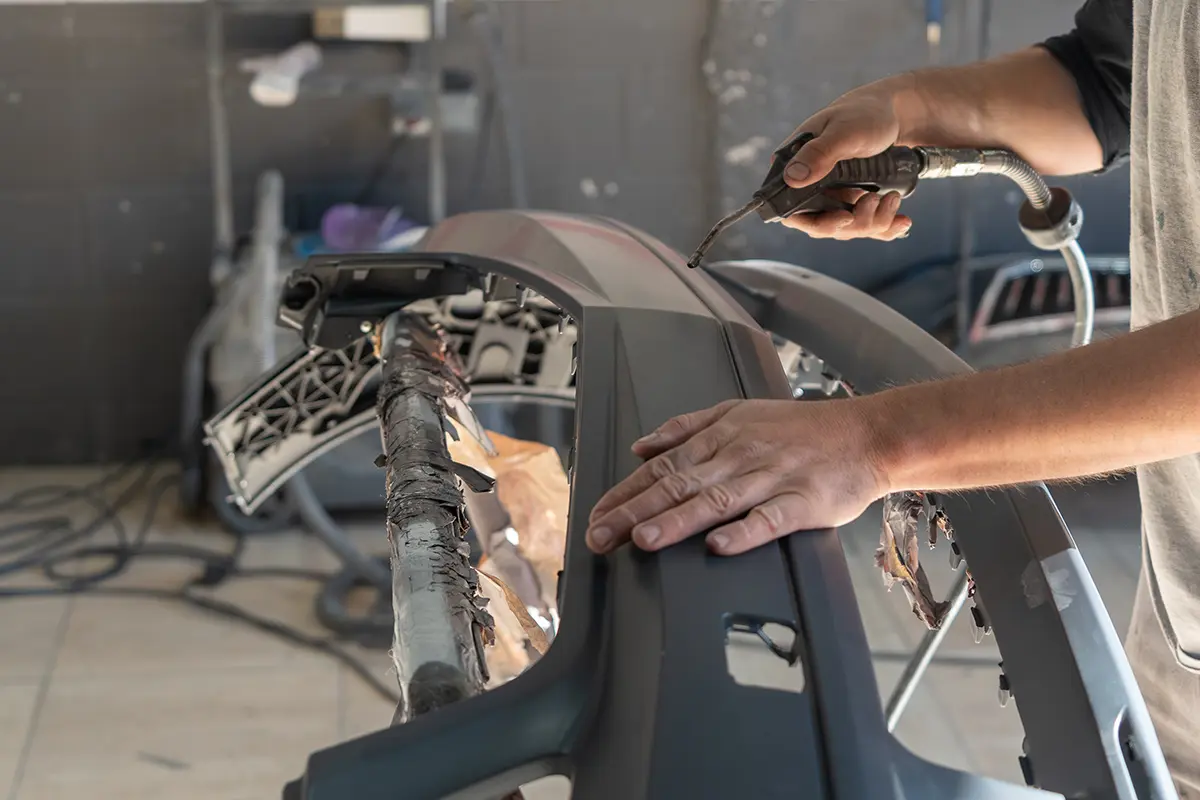 Auto body technician repairing a detached car bumper on a work stand.